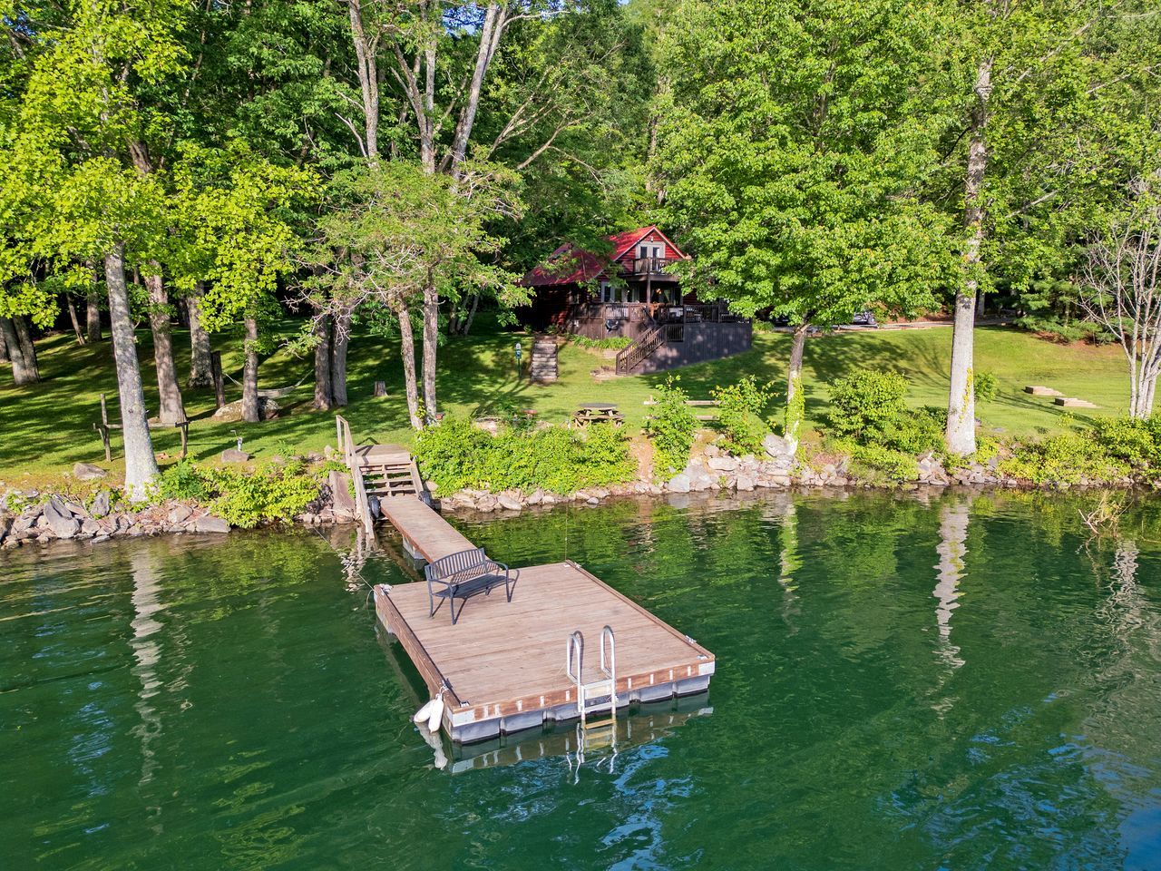 Une jetée s’avançant dans un lac, avec une plateforme en bois et une échelle, entourée d’arbres et d’un petit bâtiment en arrière-plan.