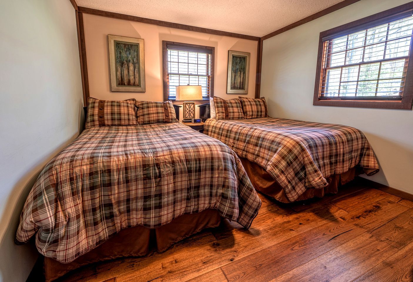 A room with two beds, wooden flooring, and a window with blinds.