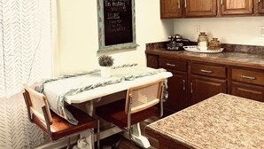 A kitchen with wooden cabinets, a chalkboard with a waffle recipe, a coffee maker, and a dining table with chairs. - Cozy Portage Lakes Hideaway (Akron)