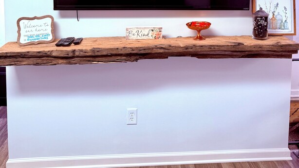 A flat-screen TV mounted on a wall, a wooden shelf with a sign, a small decorative item, and a framed picture. - Cozy Portage Lakes Hideaway (Akron)