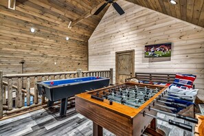 A room with a foosball table, a pool table, and a television displaying a sports event. - Fantastic Cabin Nestled Amidst Trees and Hot-tub Provided in Sevierville, Tennessee (Sevierville)