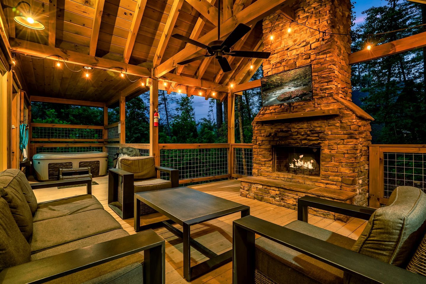 An outdoor patio with stone fireplace, wooden furniture, and string lights.