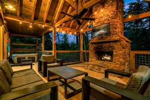 Patio esterno con camino in pietra, mobili in legno e luci decorative.