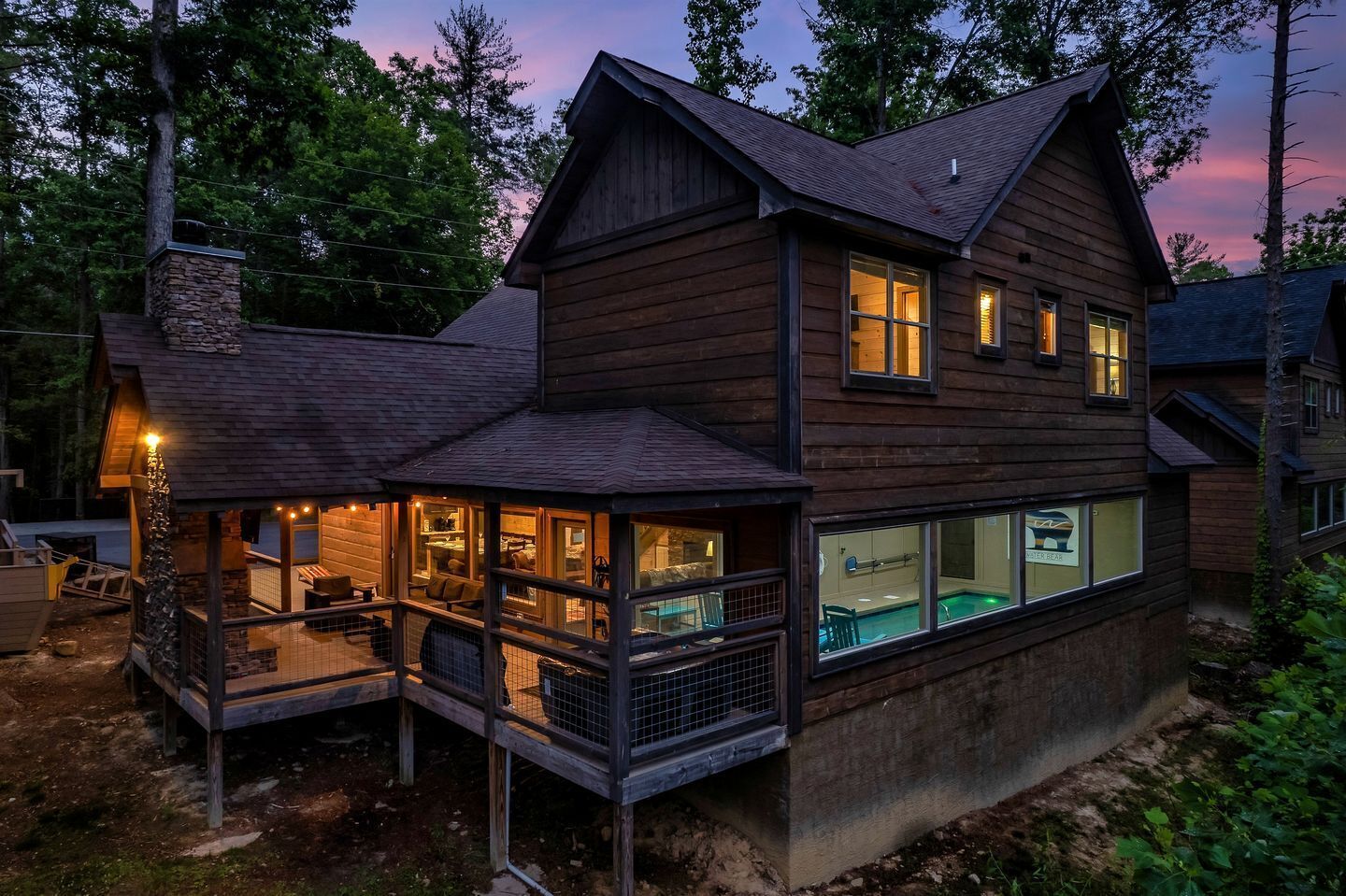 A two-story wooden house with a covered porch, a swimming pool, and a stone chimney.