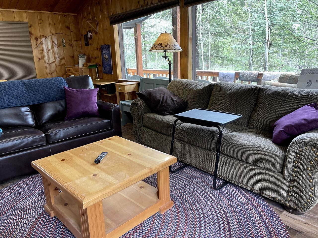 A cozy cabin interior with a wooden floor, two sofas, a coffee table, and a window with a view of trees.