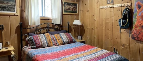 A wooden-paneled room with a bed, a nightstand, a lamp, and a coat rack.