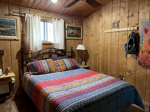 Habitació amb panells de fusta, un llit, una tauleta de nit, una làmpada i un penjador.