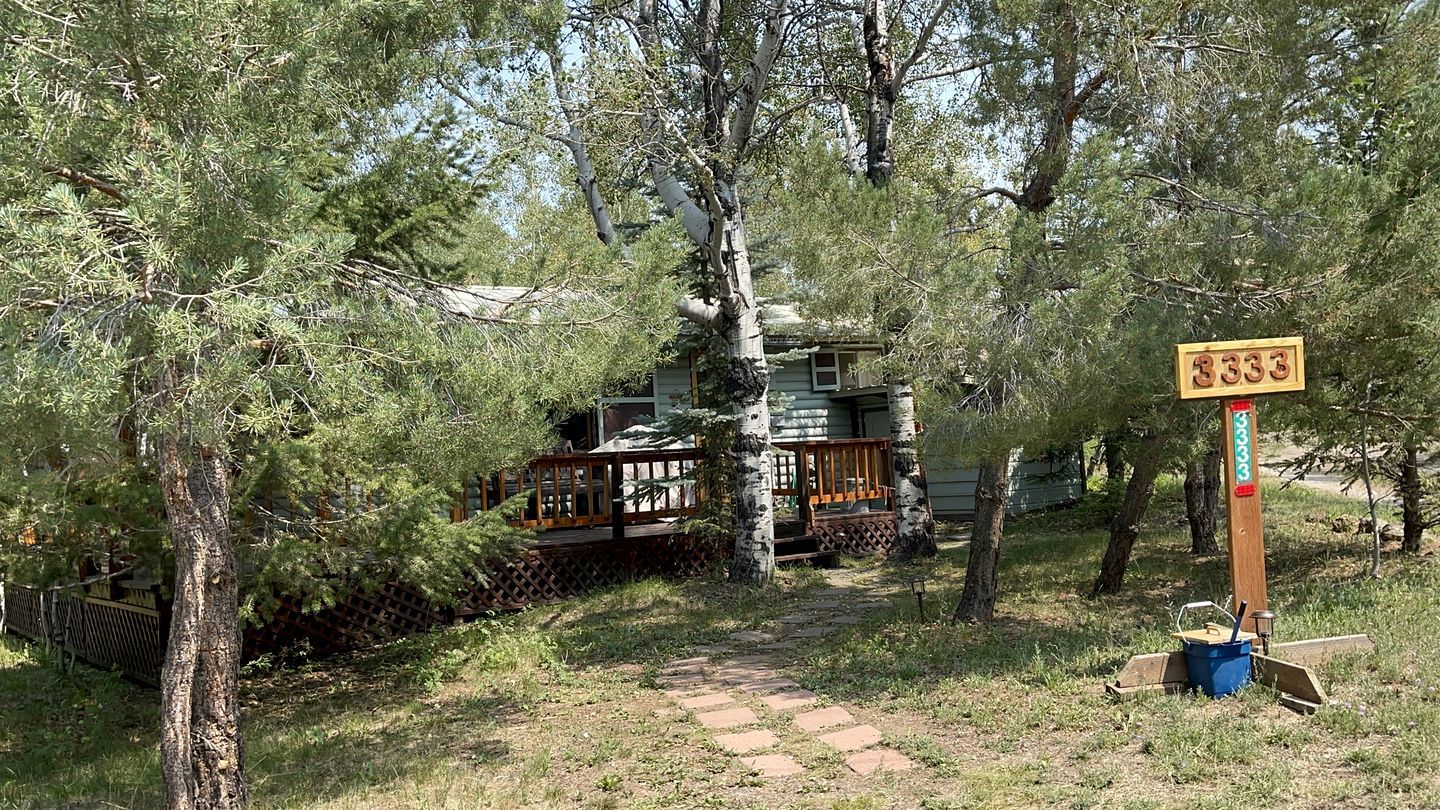 Une cabane dotée d’une terrasse en bois, entourée d’arbres et accessible par un sentier de pierres.