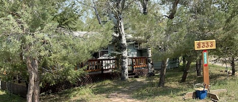 Eine Holzhütte mit einer Holzterrasse, umgeben von Bäumen und einem Steinweg, der dorthin führt.