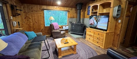 Ein gemütliches Blockhaus-Interieur mit einer Couch, einem Couchtisch, einem Kamin und einem Fernseher.