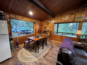 A wooden cabin interior with a dining table, chairs, a refrigerator, and a leather couch. - Cozy Secluded Cabin Surrounded by Trees near Yellowstone, Idaho (Island Park)