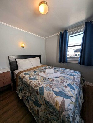 A bedroom with a bed, a nightstand, a window with curtains, and a wall-mounted light fixture. - Intimate Seaside Stay with Sunset Views in North Truro, Massachusetts (North Truro)