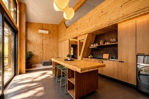A modern kitchen with a wooden island, bar stools, and built-in appliances. - Contemporary Forest Hideaway with Stunning Glass Architecture in Tracy, Tennessee (Tracy City)