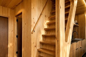 A wooden staircase with a kitchen area at the bottom. - Contemporary Forest Hideaway with Stunning Glass Architecture in Tracy, Tennessee (Tracy City)