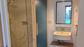 A bathroom with a glass shower enclosure, a wooden door, a white sink with a tiled backsplash, and a mirror above the sink. - Le Fournil, a quiet one-room studio near the beaches (Courtils)