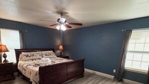 Um quarto com cama, ventilador de teto e janela com cortinas.
