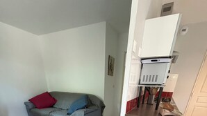 Een woonkamer met een grijze bank, een houten salontafel en een kitchenette met een witte koelkast.