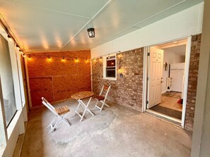 A room with a concrete floor, a brick wall, a wooden table with two chairs, and a door leading to a kitchen. - Charming Beaufort Space | Perfect 4 Extended Stays (Beaufort)