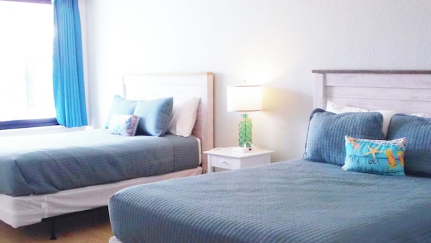 Ett hotellrum med två sängar, ett nattduksbord, en lampa och ett fönster med gardiner.