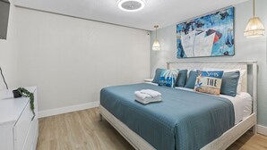 Une chambre à coucher avec un lit, un luminaire au plafond, un tableau accroché au mur et une lampe de chevet.