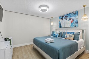 Ein Schlafzimmer mit einem Bett, einer Deckenleuchte, einem Wandbild und einer Nachttischlampe.