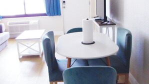 Una stanza con un tavolo rotondo, sedie blu, un divano bianco, un televisore su un mobile e una finestra con tende.