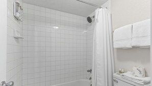 Un bagno con piastrelle bianche, una vasca, un soffione della doccia, un water e un portascopevoli.