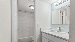 Un bagno con un mobile lavabo bianco, uno specchio con illuminazione, una vasca e una doccia.