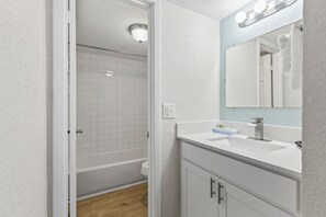A bathroom with a white vanity, a mirror with lights, a bathtub, and a shower. - Direct Oceanfront Daytona Beach Condo | Full Kitchen | Beach Access (Daytona Beach Shore)