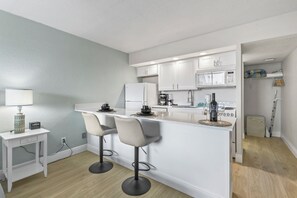 A modern kitchen with white cabinets, a central island with bar stools, a microwave, and a coffee maker. - Direct Oceanfront Daytona Beach Condo | Full Kitchen | Beach Access (Daytona Beach Shore)