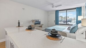 Una camera d'albergo con angolo cottura, un letto con biancheria azzurra, una TV e vista sulla strada.