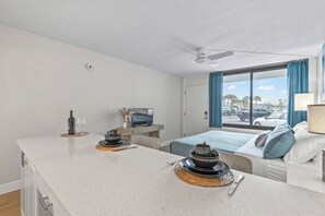 Ein Hotelzimmer mit einer Küchenzeile, einem Bett mit blauer Bettwäsche, einem Fernseher und Blick auf die Straße.
