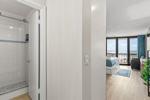 Ein modernes Hotelzimmer mit Dusche, einem Balkon mit Aussicht, einem Schreibtisch und einem Bett.