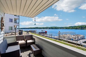 A balcony with wicker furniture, a view of a lake, a dock with boats, and a building with a balcony. - Loon Lodge - Lakefront at Lighthouse Cove (Wisconsin Dells)
