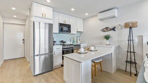 Una cocina moderna con armarios blancos, electrodomésticos de acero inoxidable y una isla central con taburetes.