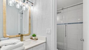 Un baño con lavamanos blanco, un espejo grande y una cabina de ducha con paredes de vidrio.