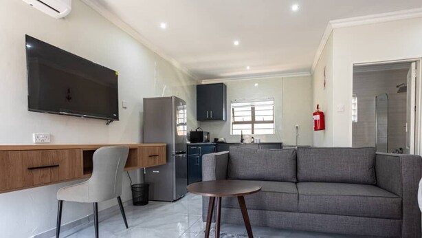 A modern living room with a flat-screen TV, a grey sofa, a wooden desk, and a small round table.