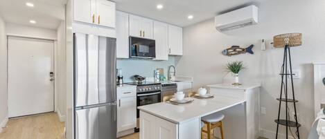 Una cocina moderna con armarios blancos, electrodomésticos de acero inoxidable y una isla central con taburetes.
