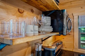 Une cuisine avec des murs en bois, un réfrigérateur en acier inoxydable et une étagère où sont rangés des verres transparents, des tasses blanches et un verre à vin.