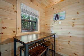 A wooden cabin interior with a window, a painting, and a table. - Charming Forest Cabin with Hot Tub & Covered Porch in Mentone, Alabama (Mentone)