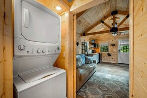 Un intérieur compact en bois comprenant un appareil combiné lave-linge et sèche-linge, un canapé et un coin cuisine.