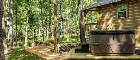 Una cabaña con terraza, bañera de hidromasaje y zona boscosa.