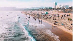 Une plage avec des gens, une tour de surveillance des sauveteurs et des bâtiments en arrière-plan.