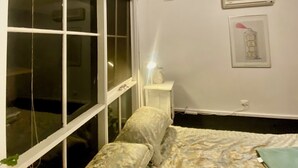 Ein Schlafzimmer mit Oberlichter, einem Bett mit gemusterten Betttextilien, einem Nachttisch mit Lampe und einer Wand-Klimaanlage.
