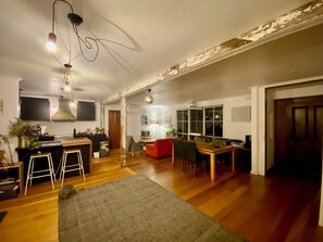 A spacious living area with a kitchen, dining table, and bar stools. - Funky house close to Castlemaine, surrounded by extensive gardens and bushland. (Golden Point)