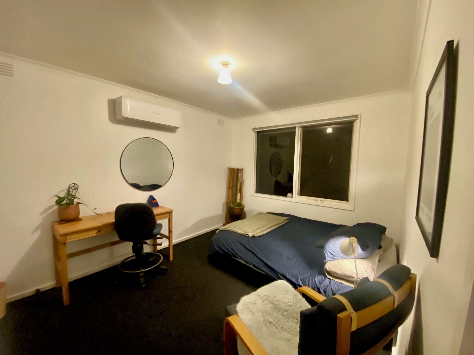 A small, well-lit room with a bed, desk, chair, and a window.