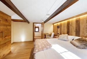 Ein Schlafzimmer mit Holzboden, einem Bett mit gemusterten Betttextilien, einem Schreibtisch und einem Stuhl.