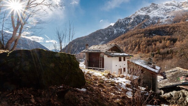 Uma cabana rústica na montanha com fachada de madeira, chaminé e cerca branca.