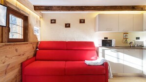 Um sofá vermelho num quarto com paredes de madeira e uma área de cozinha.
