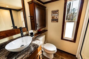 A bathroom with a white sink, a toilet, and a cabinet. There is a window with a view of trees. - Quiet Nature Retreat Perfect for Unwinding & Outdoor Moments in Monteagle, Tennessee (Monteagle)
